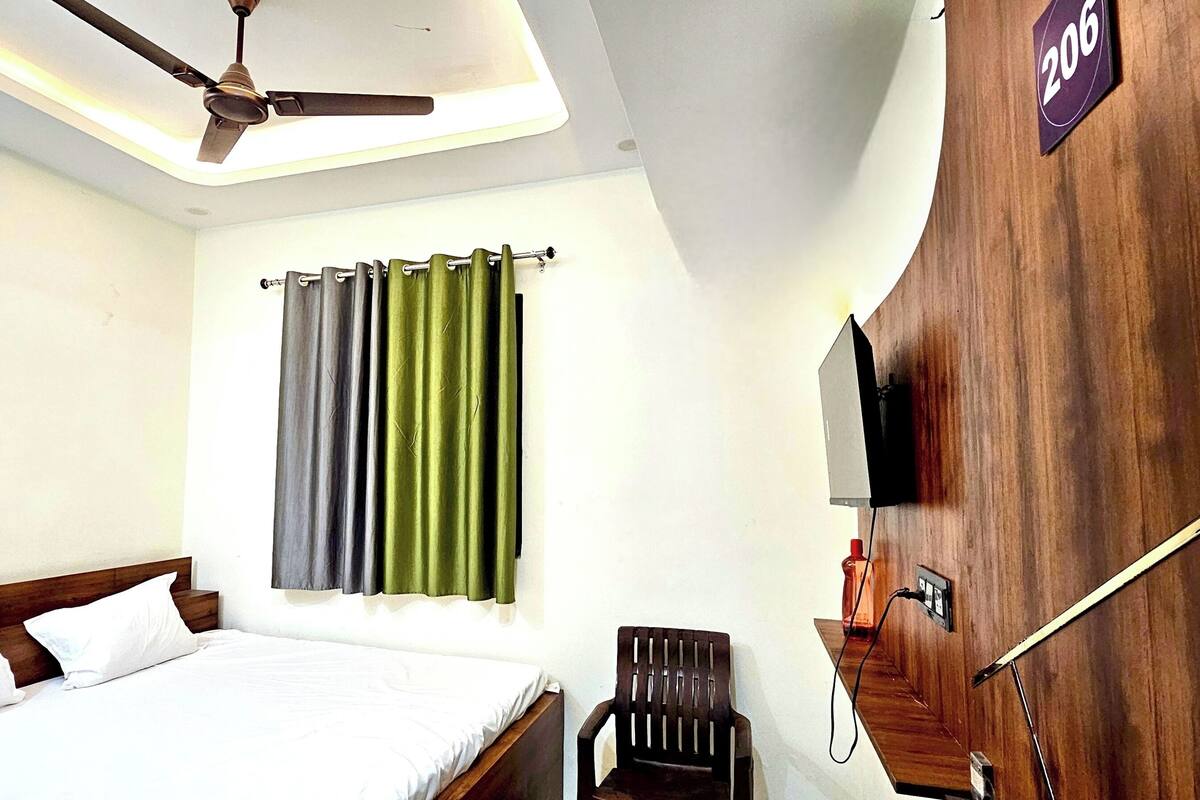 Habitación de hotel con cama, una silla, ventilador de techo, televisor montado en pared de madera y cortina.