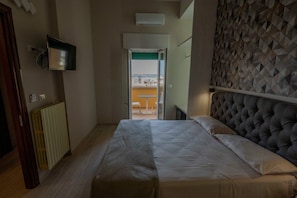 Ein Schlafzimmer mit Bett, Heizkörper, Fernseher und Blick durch eine offene Tür.