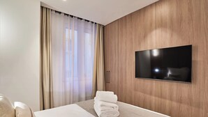 Hotellihuone, jossa on sänky, seinälle asennettu televisio ja ikkuna, jossa on verhot.