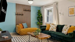 Una sala de estar con un sofá, una mesa de centro, un televisor, una planta y una ventana con cortinas.