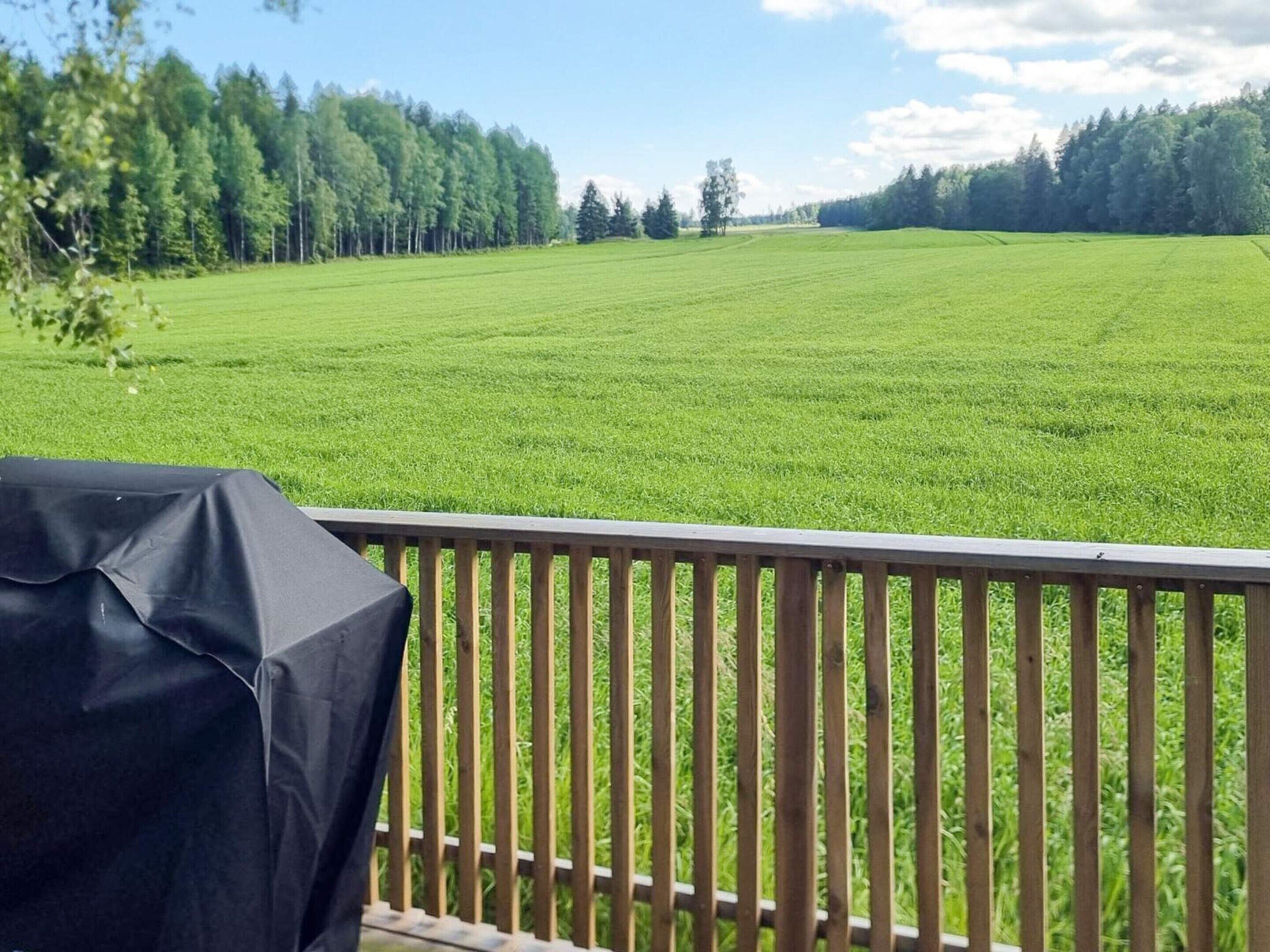 A deck with a view of a green field and trees.