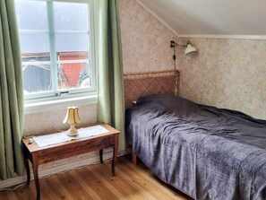 Ein kleines Schlafzimmer mit einem Einzelbett, einem Nachttisch mit Lampe, einem Fenster mit Vorhängen und einer Wand mit Muster.