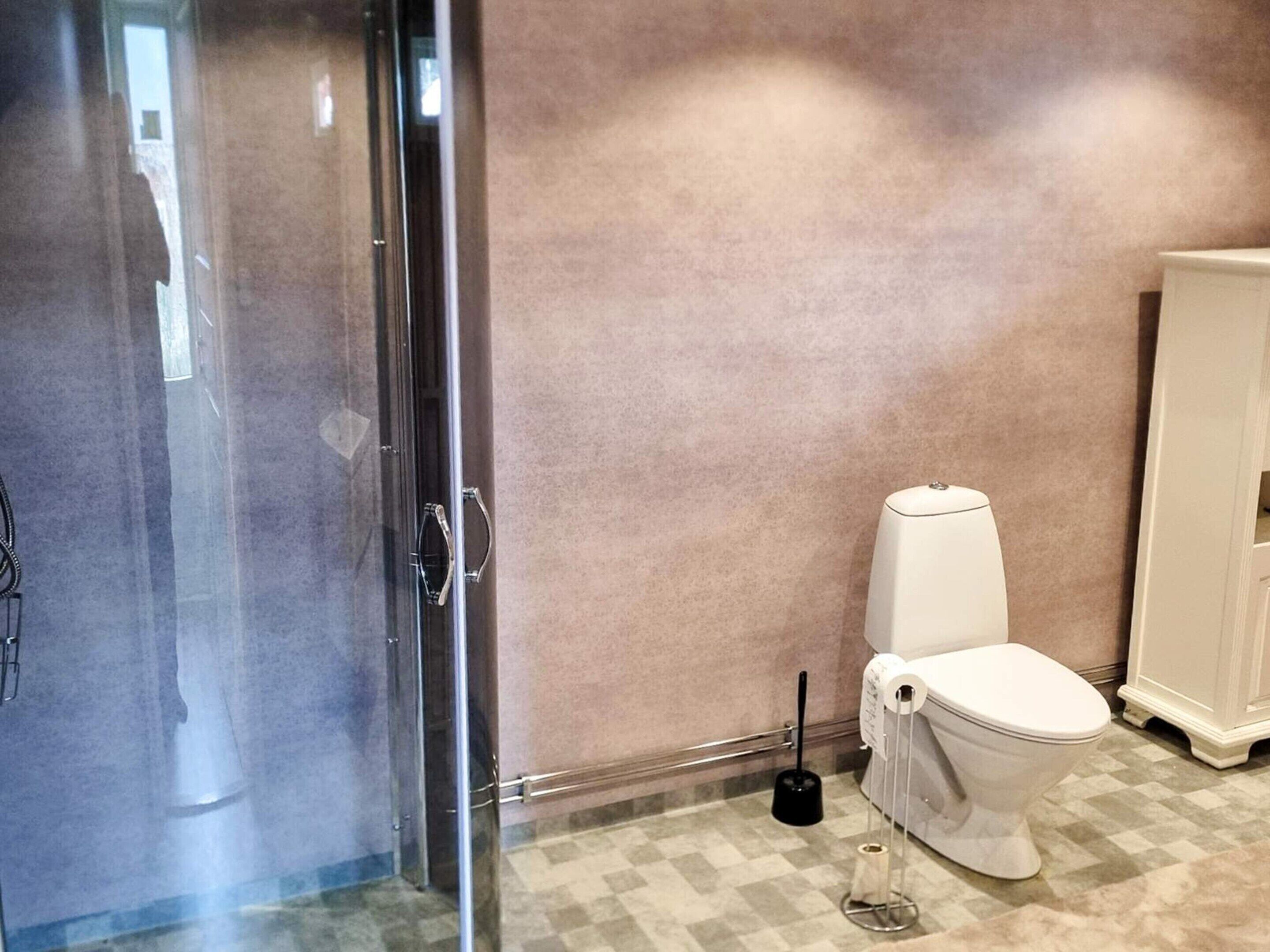 A bathroom with a glass shower enclosure, a toilet, and a white cabinet.