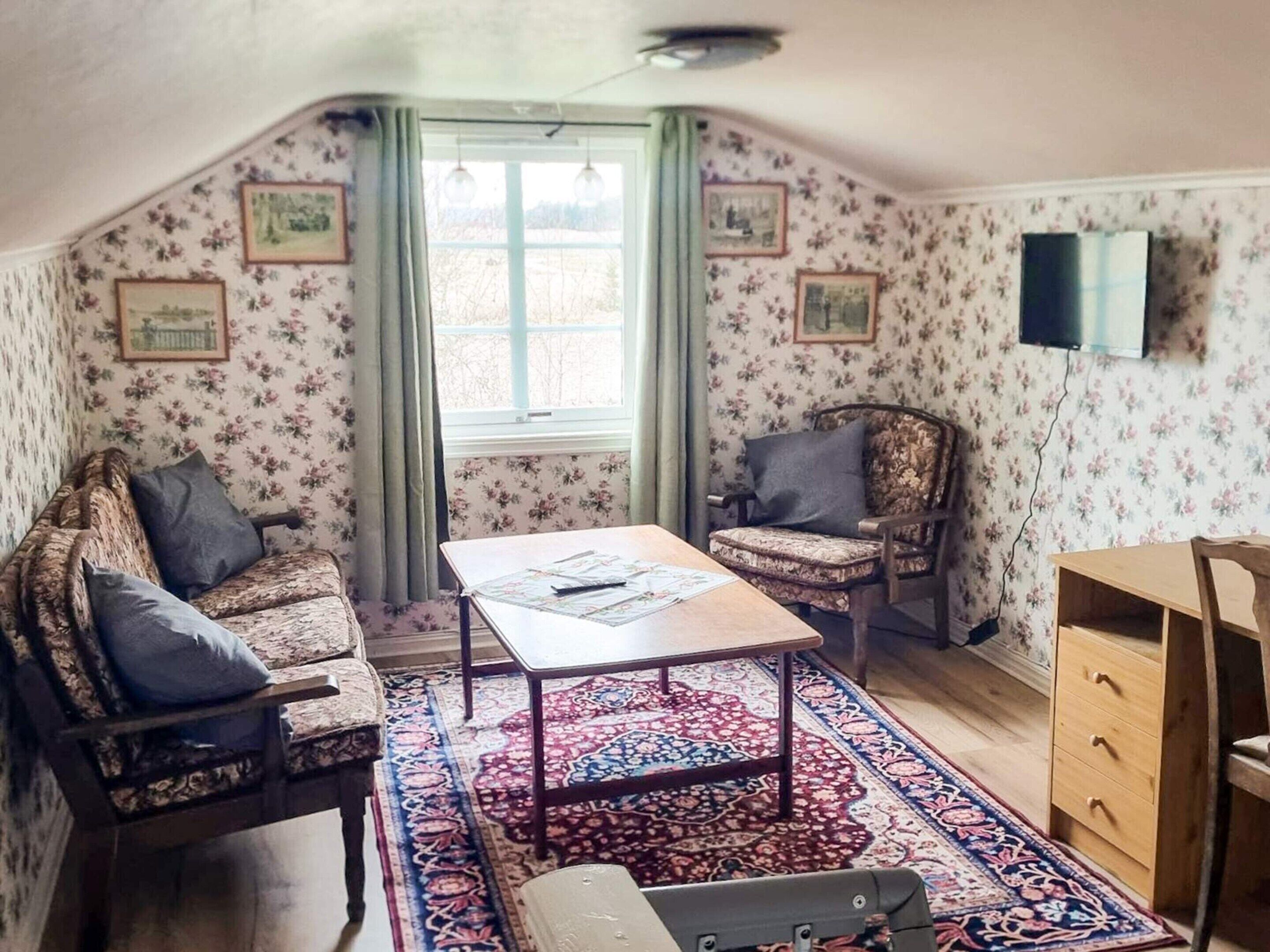 A room with a sofa, armchair, table, and a TV on the wall.