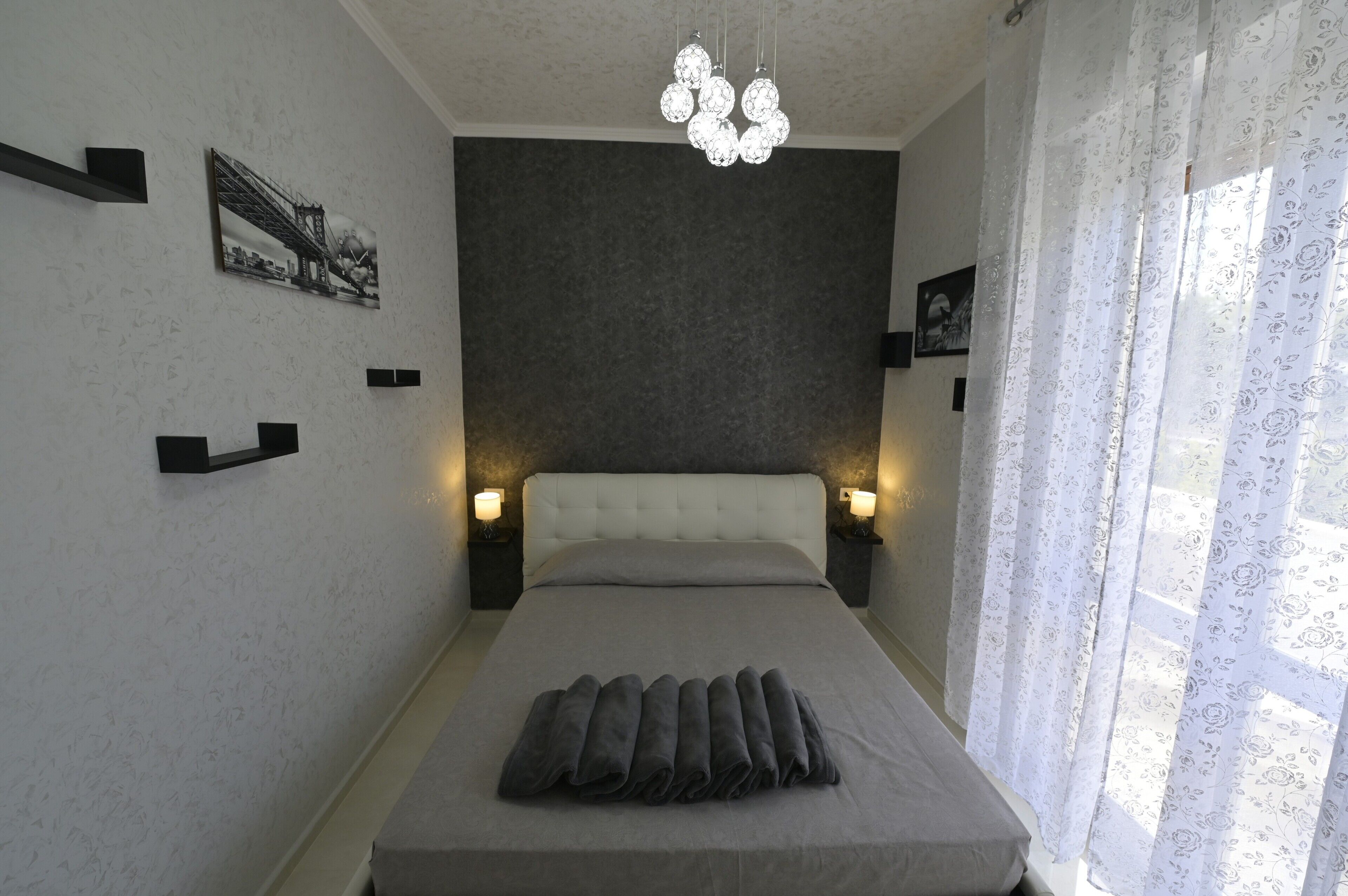 A bedroom with a bed, bedside lamps, a chandelier, and a window with curtains.