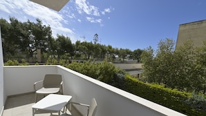 A balcony with two chairs and a table, overlooking a green area with trees and a building.
