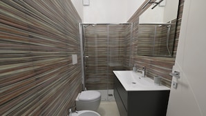 A modern bathroom with striped tile walls, a toilet, a bidet, and a sink with a mirror.