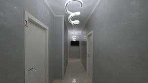 A hallway with a modern light fixture, a flat-screen TV mounted on the wall, and a door at the end.
