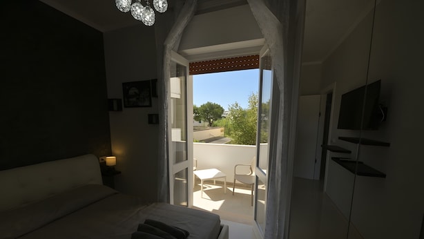 A bedroom with a bed, a nightstand, a TV, and a balcony with a chair and table.