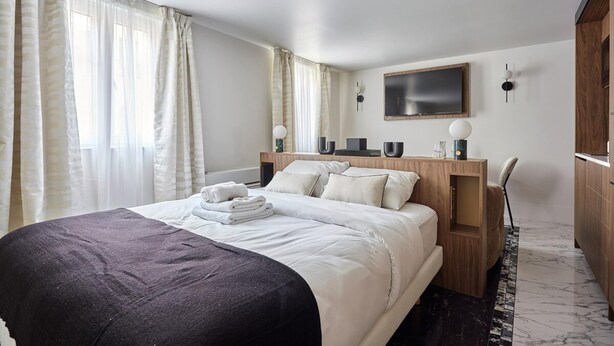 A modern hotel room with a large bed, wooden headboard, a flat-screen TV, and a marble floor. - Beautiful Studio With AC - Louvre Palais Royal (Paris)