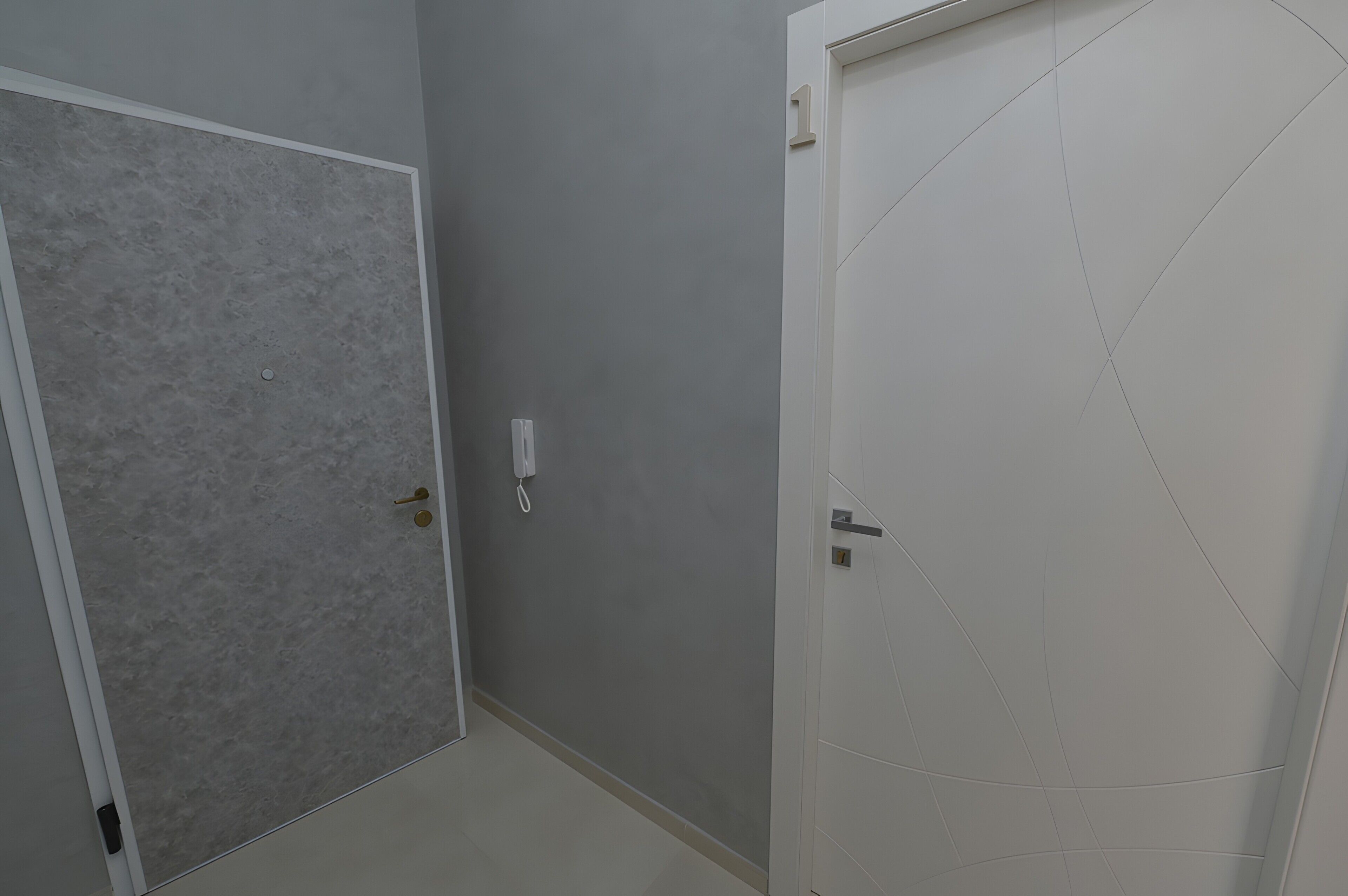 A hallway with two doors, one with a textured gray wall and the other with a plain white wall.