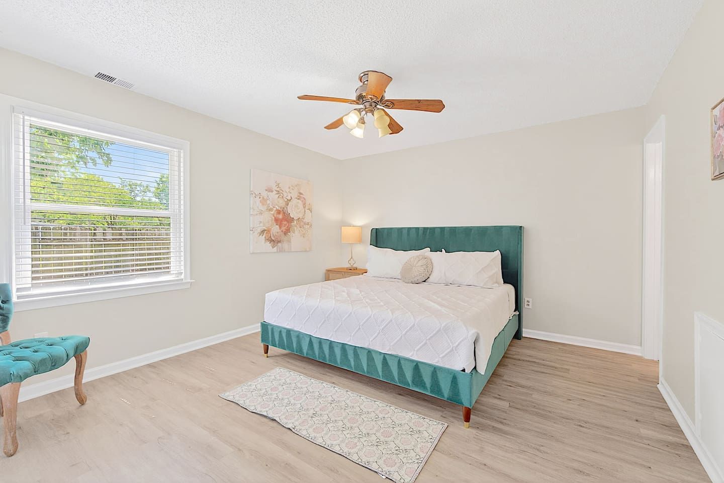 A bedroom with a bed, a ceiling fan, a window with blinds, a chair, and a rug.