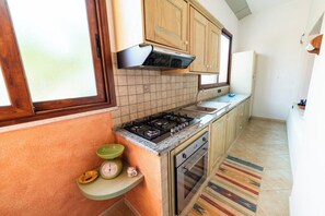A kitchen with wooden cabinets, a gas stove, a built-in oven, and a window. - Timeless house, 10 minutes from the sea - Quiet & Roomy (Riola Sardo)