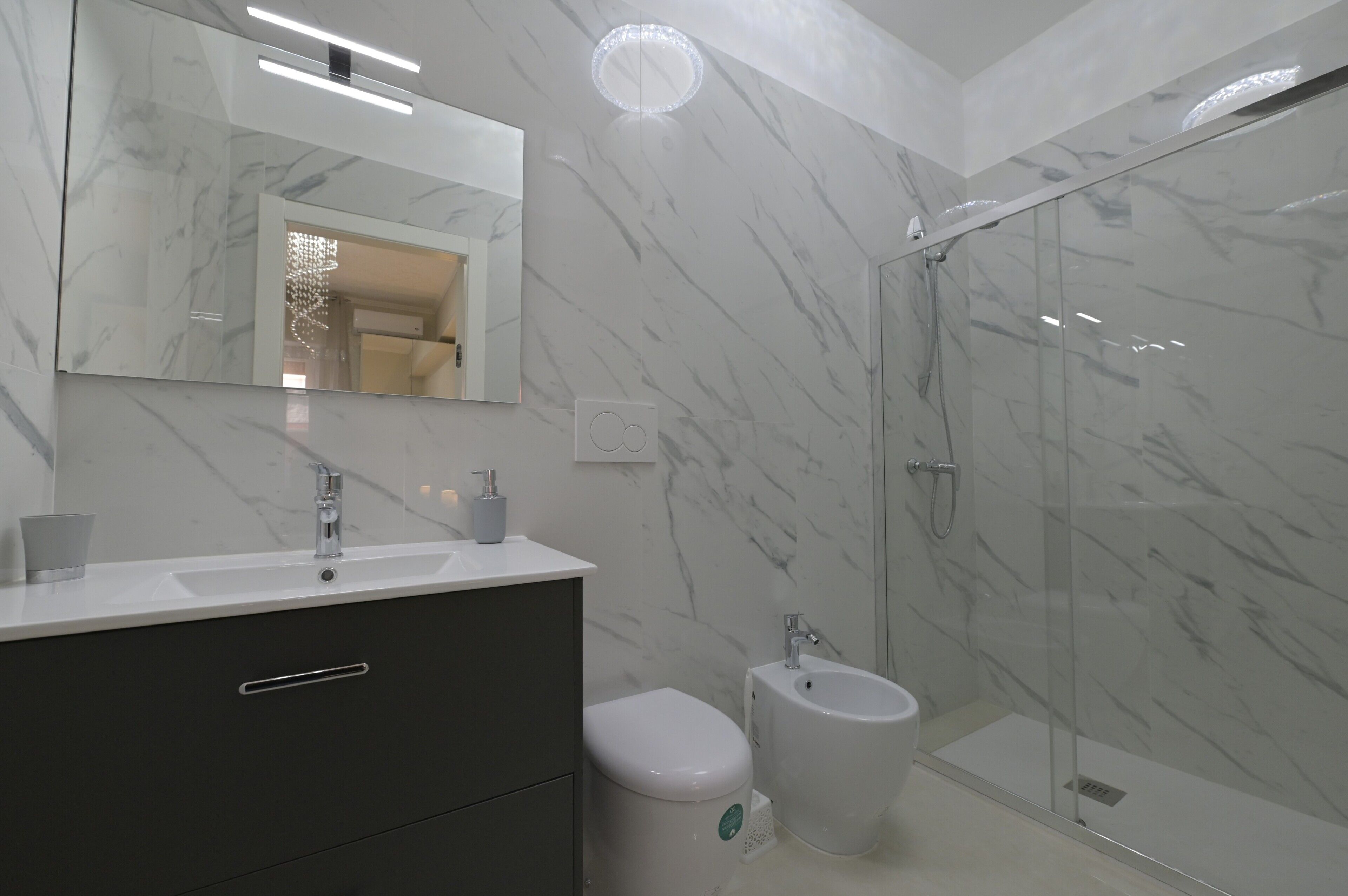 Een moderne badkamer met een marmeren wand, een grote spiegel, een wastafel, toilet en een douche met glazen wanden.