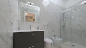 Une salle de bain moderne avec un mur en marbre, un meuble-lavabo de couleur foncée, une cabine de douche en verre et des toilettes.