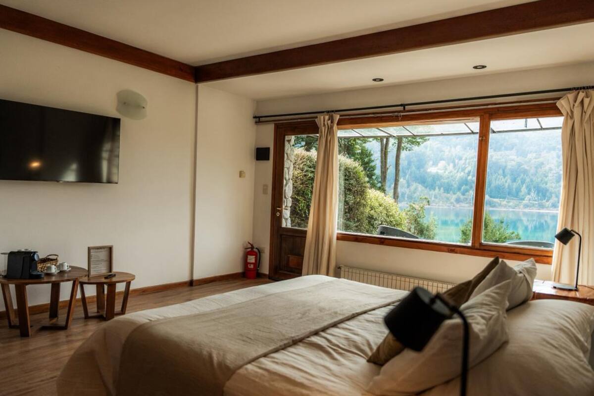 Un dormitorio con cama, televisor, una mesa con tetera y vista a un lago.