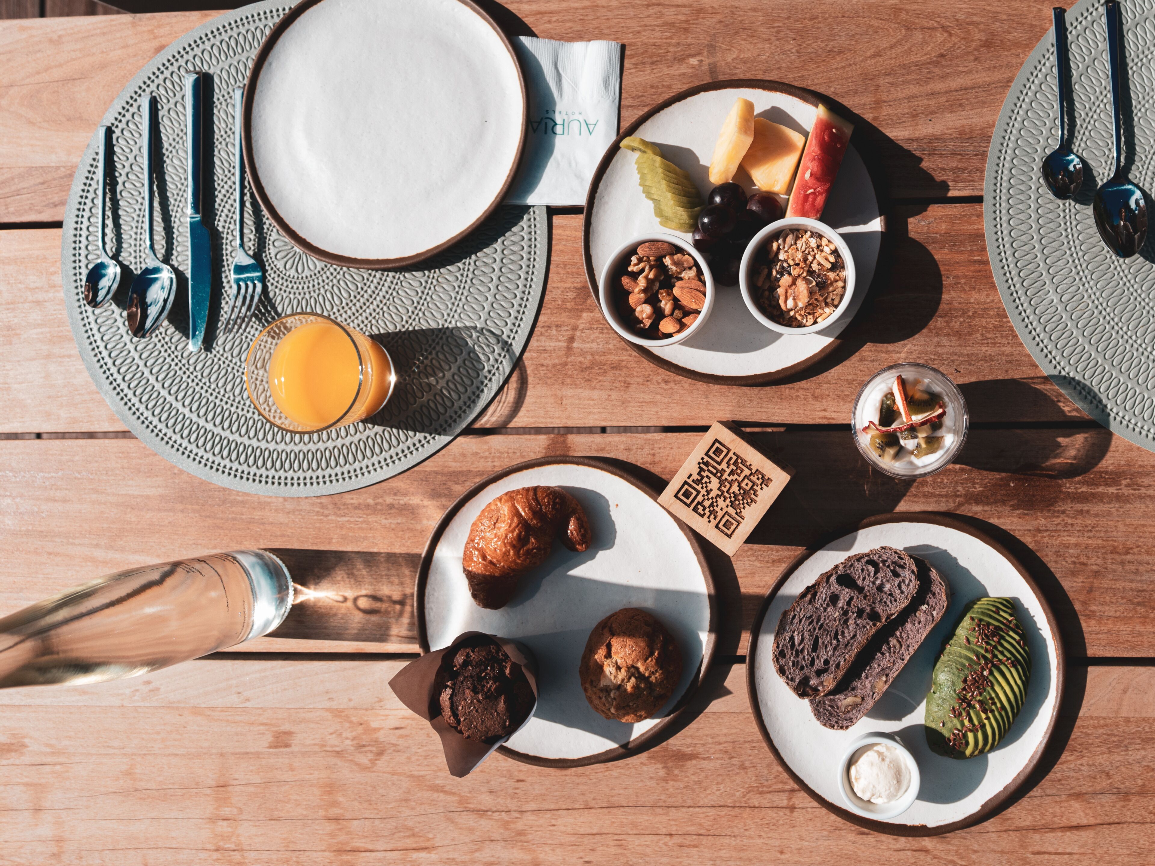 Una mesa servida con platos, cubiertos, un vaso de jugo de naranja y diferentes alimentos.