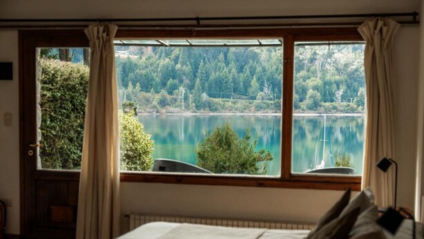 Un dormitorio con un amplio ventanal con vistas a un lago y un bosque.