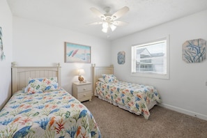 A bedroom with two single beds, a ceiling fan, a nightstand with a lamp, and artwork on the walls. - JL S-2B - Oceans 11 - The Sands Condos - Oceanfront - Community Pool (Kill Devil Hills)