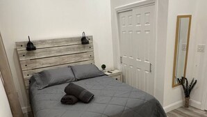 Um quarto com cama, cabeceira de madeira, mesas de cabeceira, uma porta e um espelho.