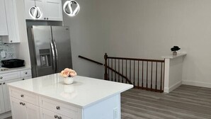 Cozinha moderna com armários brancos, uma geladeira de aço inoxidável e uma ilha central branca com um vaso de flores.