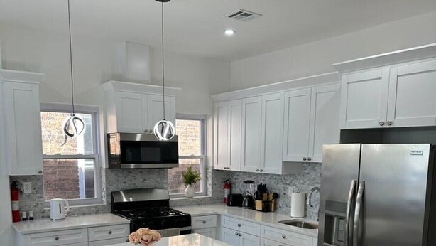 Uma cozinha moderna com armários brancos, uma geladeira de aço inoxidável e uma ilha central.