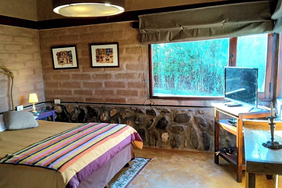 A bedroom with a bed, a desk, a window with a view, and two framed pictures on the wall.