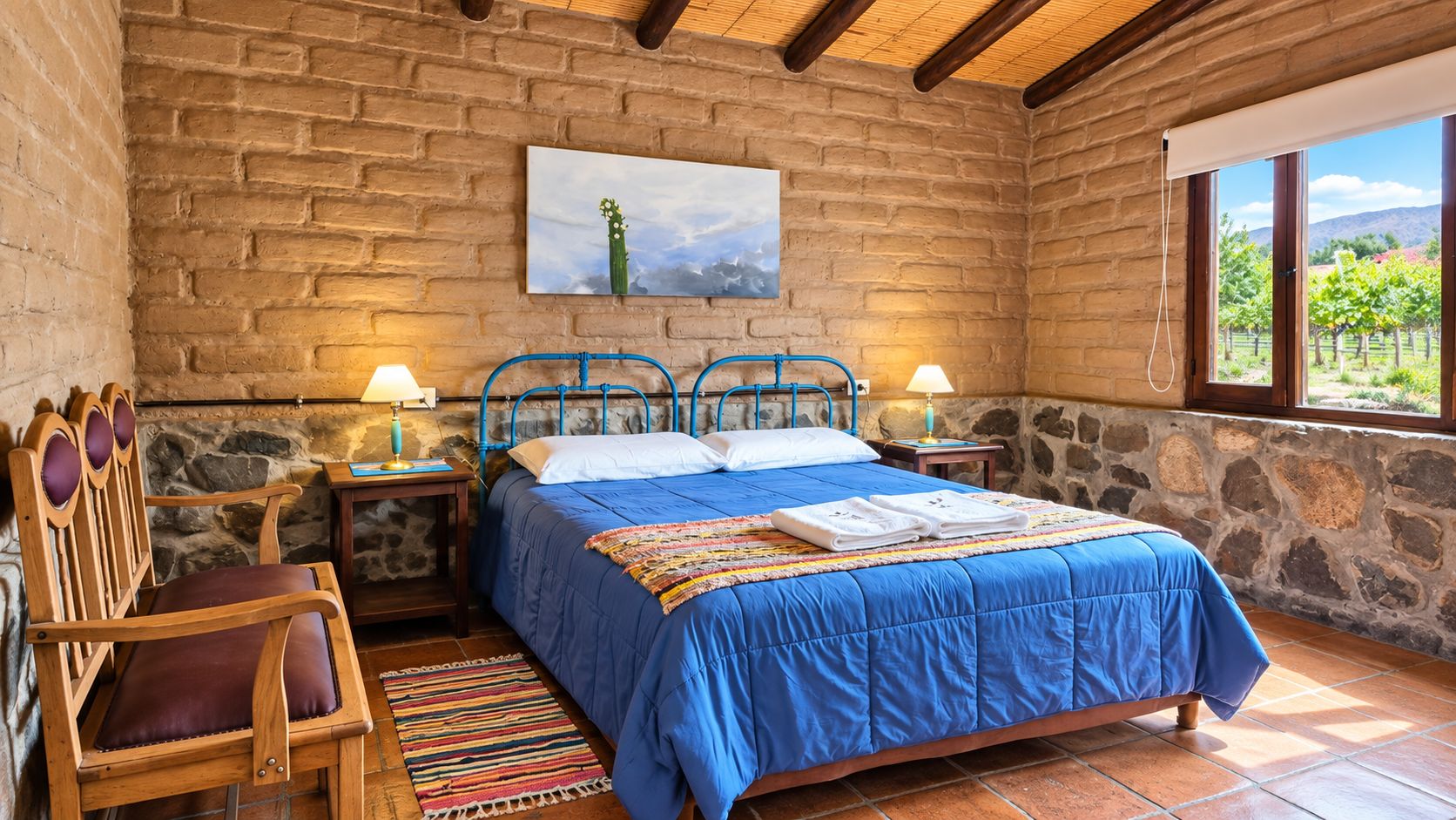 A rustic bedroom with a stone wall, a bed with blue bedding, a wooden chair, and a painting of a cactus.