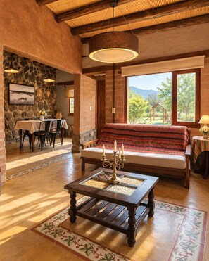 Un interior acogedor con una pared de piedra, un comedor, un sofá con un plaid estampado y una mesa de centro con un candelabro.