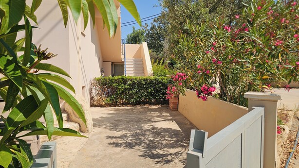 A narrow alleyway with a beige wall, a gate, and a small garden with pink flowers. - Casa Elysia 2BR Beach & Pool  (Maleme)