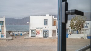 A coastal building with a sign 'Costa Famosa,' outdoor seating, and a view of the sea and mountains. - Vacation Home 'Casa Montaña Clara Famara' with Mountain View and Wi-Fi (Caleta de Famara)