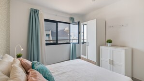A bedroom with a bed, curtains, a window, a cabinet, and a plant. - Vacation Home 'Casa Montaña Clara Famara' with Mountain View and Wi-Fi (Caleta de Famara)