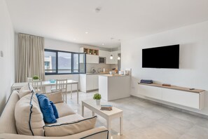Una sala de estar moderna con un sofá, una mesa de comedor y una zona de cocina con un televisor montado en la pared.