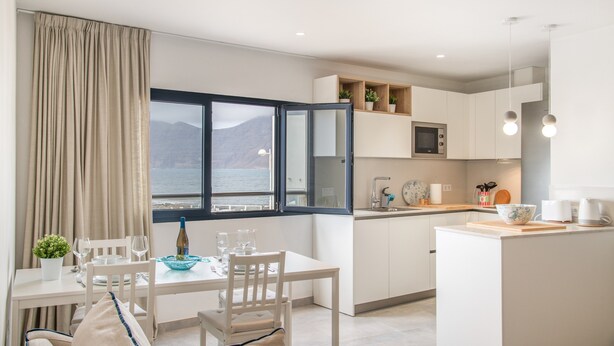 A modern kitchen with a dining area, a view of the sea, and a small island. - Vacation Home 'Casa Montaña Clara Famara' with Mountain View and Wi-Fi (Caleta de Famara)