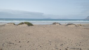 A beach with sand, rocks, and the ocean. - Vacation Home 'Casa Montaña Clara Famara' with Mountain View and Wi-Fi (Caleta de Famara)