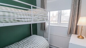 Habitación con literas, una ventana, un radiador y una mesita de noche con lámpara.