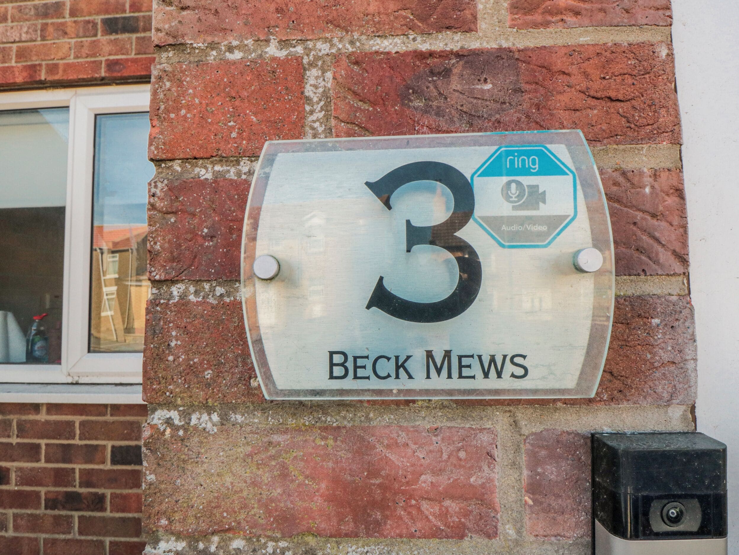 Eine Hausnummernschild mit der Aufschrift '3' und 'BECK MEWS' an einer Ziegelwand.
