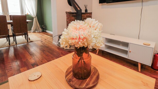Un salón con una mesa de madera, un jarrón de flores, una chimenea, un televisor y una zona de comedor con sillas y una mesa.