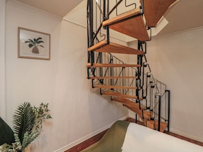 A spiral staircase with a wooden finish and metal railings, a framed plant on the wall, and a green upholstered bench. - 3 Beck Mews (Scarborough)