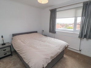 A bedroom with a bed, a nightstand, a lamp, a window with curtains, and a radiator. - 3 Beck Mews (Scarborough)