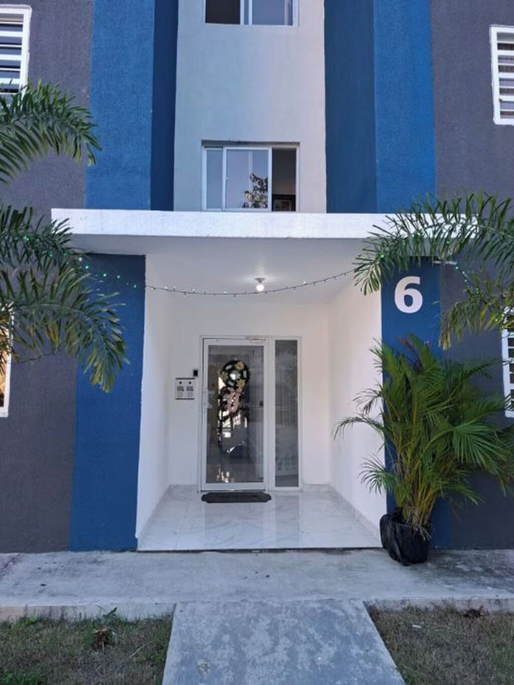 Un bâtiment moderne à la façade bleue et blanche, doté d’une entrée en verre et d’une enseigne portant le chiffre « 6 ».