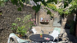 Eine Terrasse mit Gartenmöbeln, einer Steinmauer und einem Backsteinhaus im Hintergrund.