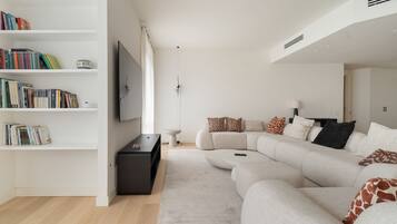 Ein modernes Wohnzimmer mit einem Ecksofa, einem Bücherregal, einem Flachbildfernseher und einem minimalistischen Design.