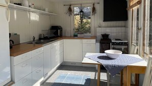 A compact kitchen with white cabinets, a wooden countertop, a small table with a bowl, a stove, and a hanging light fixture. - 4 Star Holiday Home in Musko (Muskö)