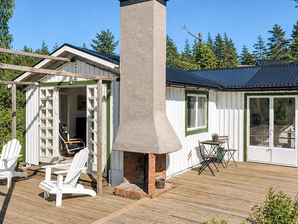 A wooden deck with Adirondack chairs, a brick fireplace, and a covered patio area. - 4 Star Holiday Home in Musko (Muskö)