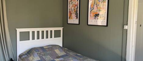 A bedroom with a white bed frame, a quilted bedspread, and two framed artworks on the wall.