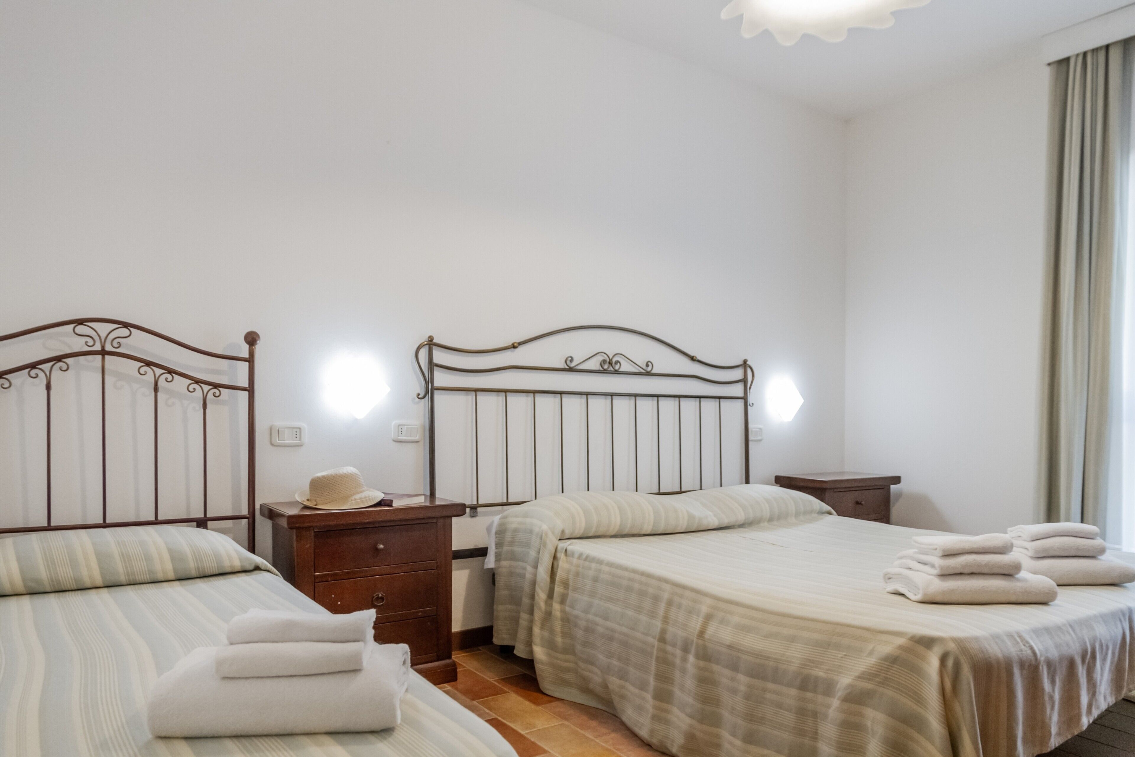 A hotel room with two beds, a nightstand, a dresser, and a window with curtains.