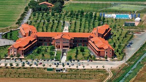 An aerial view of a large building complex with multiple red-roofed structures, surrounded by green fields and a road. - Apartment '1' Borgo San Giorgio (Grosseto)