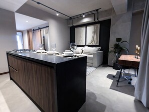 A modern kitchen with a central island, a dining area with a table and chairs, and a living space with a sofa and curtains. - Atena Urban Living | Depa premium en Col Americana (Guadalajara)