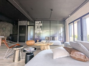 A modern living room with a large window, a round wooden coffee table, and a sofa with cushions. - Atena Urban Living | Depa premium en Col Americana (Guadalajara)